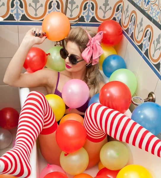 Femme blonde avec des lunettes de soleil jouant dans son tube de bain avec des ballons de couleur vive. Sensuelle fille avec blanc et rouge rayé bas avoir du plaisir dans la salle de bain, recouvert de ballons — Photo