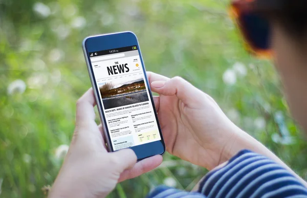 Dívka v trávě drží smartphone novinky — Stock fotografie