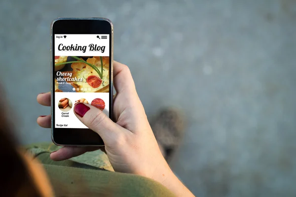 Woman walking with smartphone with cooking blog on screen — ストック写真