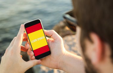 Man using his mobile phone on the coast to learn spanish