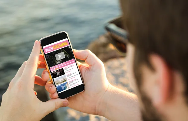 Man using his mobile phone on the coast to watch videos — Zdjęcie stockowe