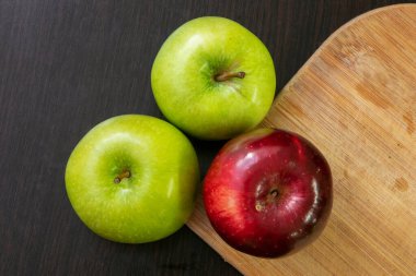 Masada üç elma, iki yeşil ve bir siyah arka planda bir kırmızı.