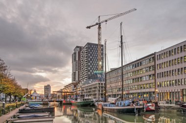 Rotterdam, Hollanda, 5 Kasım 2020: Wijnhaven limanı üzerinde şalopalar, tarihi mavnalar, modern mimari ve bir inşaat vinci ile dramatik gökyüzü