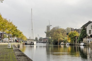 Schiedam, Hollanda, 23 Ekim 2020: Buitenhaven (dış liman) çevresindeki modern ve geleneksel endüstrilerin bir karışımı yelkenli ve Nolet yel değirmeni ile
