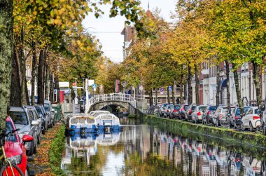 Delft, Hollanda, 11 Kasım 2020: Eski kentteki Koornmarkt Kanalı 'nda sonbahar renklerinde turist tekneleri, park edilmiş arabalar ve ağaçlar