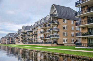 Voorschoten, Hollanda, 3 Ocak 2021: Krimwijk mahallesindeki bir kanal boyunca post-modern eklektik tarzda tuğla cepheli apartman blokları.