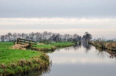 Hollanda 'da Haastrecht ve Oudewater arasındaki Tiendweg yürüyüş yolu boyunca uzanan geniş bir polderhendeğe yansıyan bulutlar ve ağaçlar Aralık ayında soğuk ama rüzgarsız bir günde