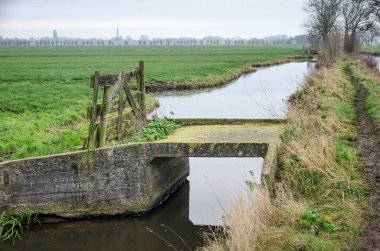 Hollanda 'da Tiendweg yürüyüş yolu boyunca bir polder hendeği boyunca uzanan eski ve yıpranmış beton bir köprü.