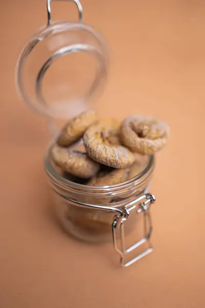 Kurumuş incirler cam bir kavanozun içinde turuncu bir arka planda yatıyor.