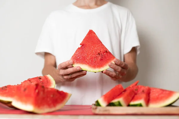 Beyaz arka plandaki bir adamın ellerinde bir karpuz parçası.