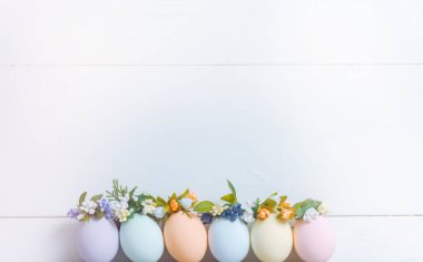 Paskalya konsepti. Pastel renklerle boyanmış Paskalya yumurtaları yumurta tepsisinde, üzerinde çelenkler var. Hafif arkaplan, metin için yer.