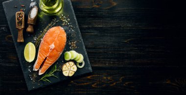 Somon bifteği kızartılmaya hazır koyu arkaplanda malzemeler var.