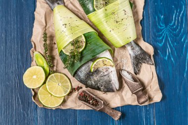 İki taze çiğ dorado balığı, palmiye yapraklarına sarılmış, biber ve büyük gimolais tuzu karışımı serpiştirilmiş, limon ve dilimlenmiş, pişirilmeye hazır. İki kişilik yemek konsepti