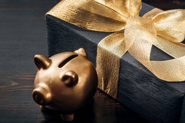 Siyah bir kağıda sarılmış ve yanında altın bir kurdeleyle bağlanmış bir hediye duruyor. Altın bir domuz kumbarası.