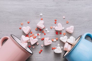 İki kupa mavi ve pembe yan yatar, küçük şeker kalpler ve lokum kalpler dökülür