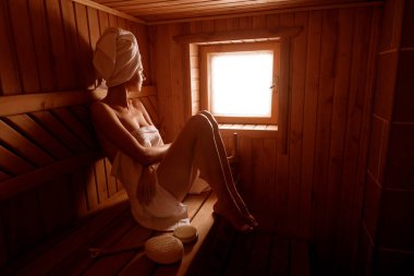 girl in a spa treatment in a traditional sauna with a brush for skin and a washcloth. relaxes wrapped in a white towel clipart