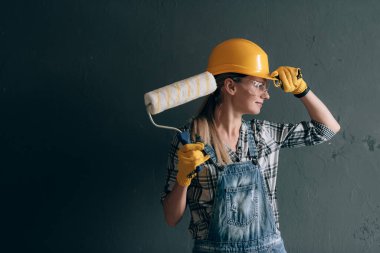 İnşaat kasklı, eldivenli, gözlüklü ve tulumlu iradeli bir kadın evde tamir ve inşaat işiyle meşgul. Güçlü ve bağımsız kadın kavramı