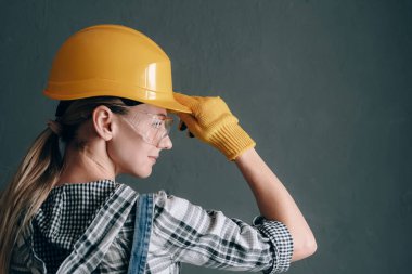 İnşaat kasklı, eldivenli, gözlüklü ve tulumlu iradeli bir kadın evde tamir ve inşaat işiyle meşgul. Güçlü ve bağımsız kadın kavramı