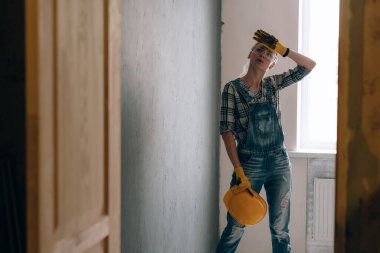 İnşaat kasklı, eldivenli, gözlüklü ve tulumlu iradeli bir kadın evde tamir ve inşaat işiyle meşgul. Güçlü ve bağımsız kadın kavramı