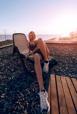 Kapalı bir mayo giymiş bir kız denizin arka planındaki bir dinlenme yerinde şafakla buluşuyor, dinleniyor ve denizin ve güneşin tadını çıkarıyor.