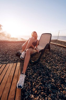 Kapalı bir mayo giymiş bir kız denizin arka planındaki bir dinlenme yerinde şafakla buluşuyor, dinleniyor ve denizin ve güneşin tadını çıkarıyor.