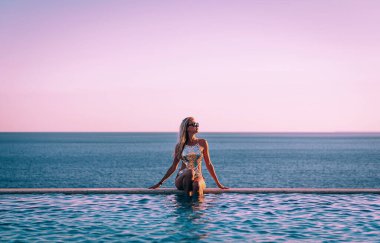 Deniz kenarındaki panoramik havuzun yanında mayo giyen kız rahatlıyor.