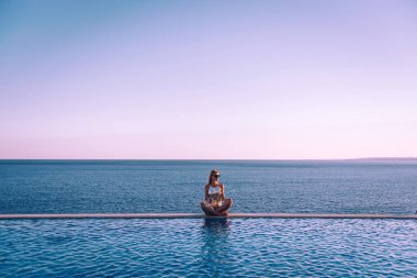 Deniz kenarındaki panoramik havuzun yanında mayo giyen kız rahatlıyor.