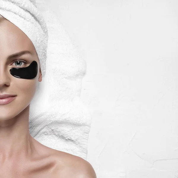 Gözlerinin altındaki deri için kozmetik maske. Başında havlu olan bir kıza göz maskesi tak.