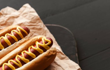 Koyu ahşap arka planda sarı Amerikan hardalıyla ızgara sosisli sandviç.