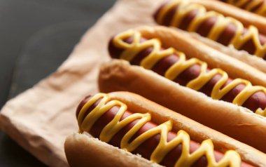 Koyu ahşap arka planda sarı Amerikan hardalıyla ızgara sosisli sandviç.