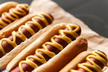 Koyu ahşap arka planda sarı Amerikan hardalıyla ızgara sosisli sandviç.