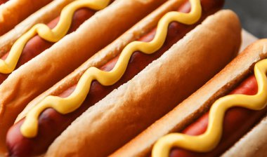 Koyu ahşap arka planda sarı Amerikan hardalıyla ızgara sosisli sandviç.