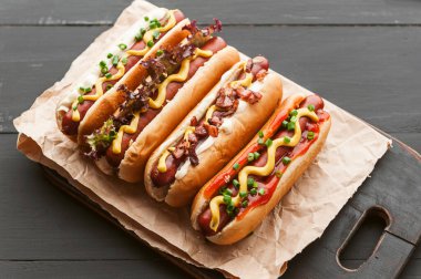 Koyu ahşap arka planda sarı Amerikan hardalıyla ızgara sosisli sandviç.