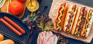 Koyu ahşap arka planda sarı Amerikan hardalıyla ızgara sosisli sandviç.