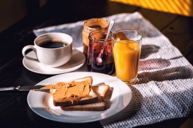 Fıstık ezmesi ve reçelli kahvaltı ve sabah güneşinde bir fincan kahve.