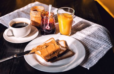 Fıstık ezmesi ve reçelli kahvaltı ve sabah güneşinde bir fincan kahve.