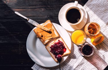 Fıstık ezmesi ve reçelli kahvaltı ve sabah güneşinde bir fincan kahve.