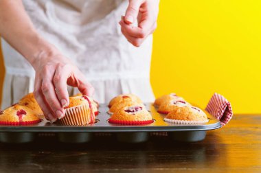 Açık sarı arka planda muffinleri olan bir aşçı.