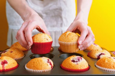 Açık sarı arka planda muffinleri olan bir aşçı.