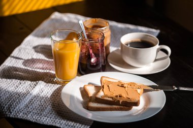 Fıstık ezmesi ve reçelli kahvaltı ve sabah güneşinde bir fincan kahve.