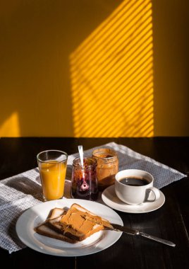 Fıstık ezmesi ve reçelli kahvaltı ve sabah güneşinde bir fincan kahve.