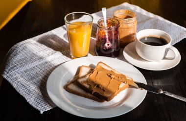 Fıstık ezmesi ve reçelli kahvaltı ve sabah güneşinde bir fincan kahve.