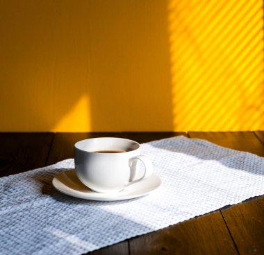 Sabah güneşinde tahta bir masanın üstünde kupa.