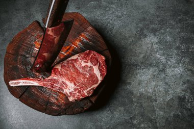 Et için ahşap bir blokta taze çiğ tamahawk bifteği ya da et için kasap baltası olan kovboy bifteği yanında kekik ile öğütülmüş biber ve kaba tuz karışımı var. taze biftek.