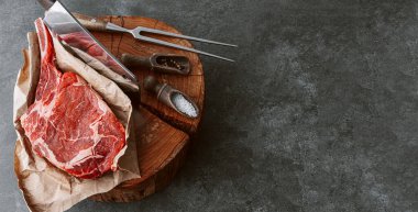 Et için ahşap bir blokta taze çiğ tamahawk bifteği ya da et için kasap baltası olan kovboy bifteği yanında kekik ile öğütülmüş biber ve kaba tuz karışımı var. taze biftek.