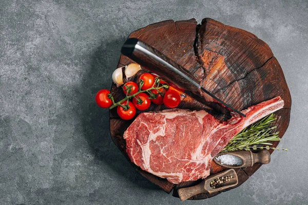 on a wooden block for meat a fresh raw tamahawk steak or a cowboy steak with a butcher\'s chopping ax for meat, next to it is a mixture of peppers and coarse salt, milled with thyme. fresh beef steak