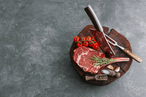 on a wooden block for meat a fresh raw tamahawk steak or a cowboy steak with a butcher\'s chopping ax for meat, next to it is a mixture of peppers and coarse salt, milled with thyme. fresh beef steak