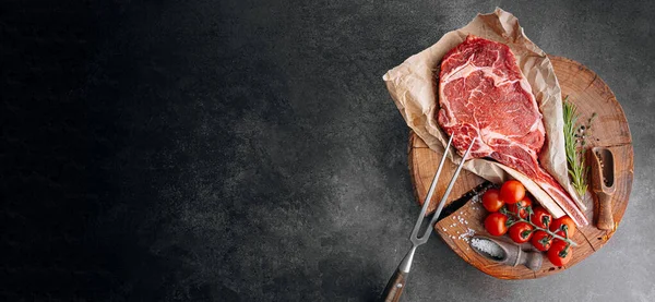 Biberiye, biberiye, kiraz, domates, biber, ahşap bir masada et baltası ile taze çiğ mermer biftek.