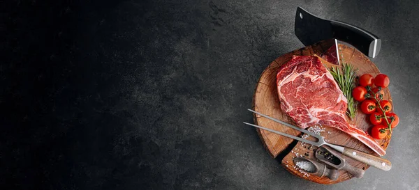 Biberiye, biberiye, kiraz, domates, biber, ahşap bir masada et baltası ile taze çiğ mermer biftek.