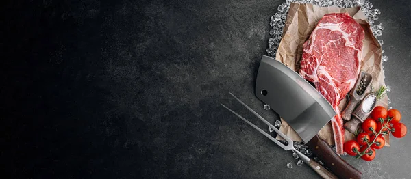 Biberiye, biberiye, kiraz, domates, biber, ahşap bir masada et baltası ile taze çiğ mermer biftek.